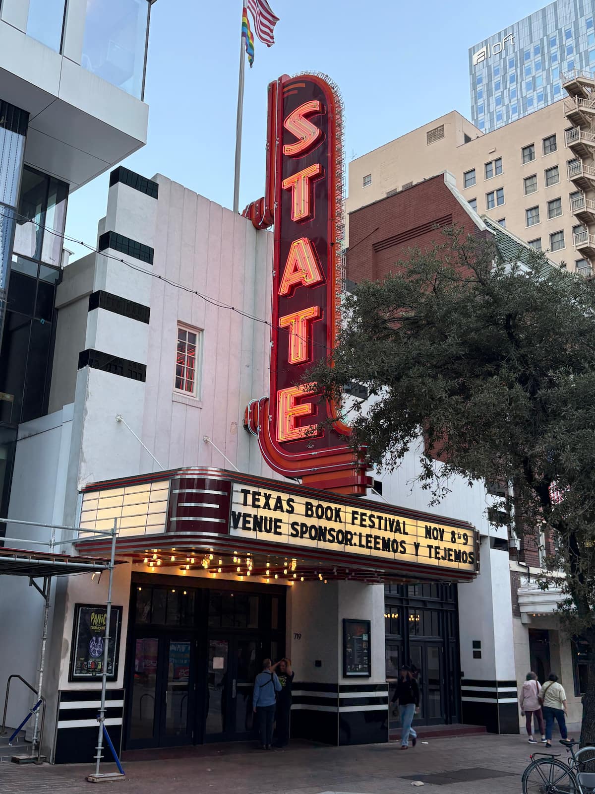 The red neon State Theatre sign in downtown Austin, Texas, illuminated above the marquee promoting the Texas Book Festival, with people walking beneath the classic entrance.